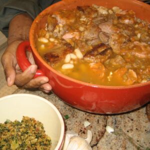 A group of nine people, possibly an Italian family, are seated around a dinner table with food in front of them, smiling for a group portrait in a cozy, home setting.