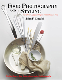 The cover of the book "Food Photography and Styling" by John F. Carafoli, featuring a skillet filled with food styling tools, including a whisk, oil, cotton swabs, paint brushes, tweezers, and a small bowl.